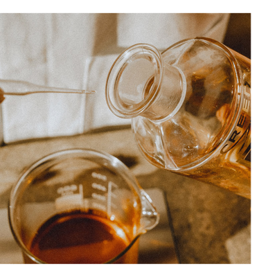 Liquid is poured from a bottle with the text CREE into a beaker containing dark liquid while a pipette is held above.