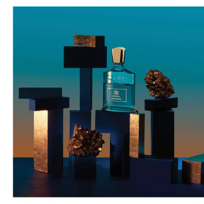 A bottle of Creed Royal Mayfair perfume is displayed among dark blocks and crystals with the text CREED ROYAL MAYFAIR visible on the label.