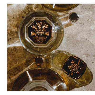 Close-up of a golden bottle, likely perfume, with a cloth-covered cap tied with a string, showing part of the bottles label with text CREED 1760.