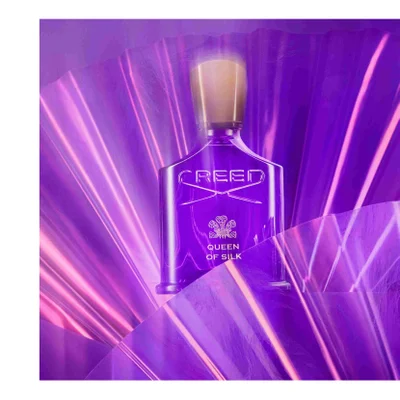 A purple Creed perfume bottle with a gold cap is centered against a backdrop of shimmering purple material, with the text CREED QUEEN OF SILK visible on the bottle.
