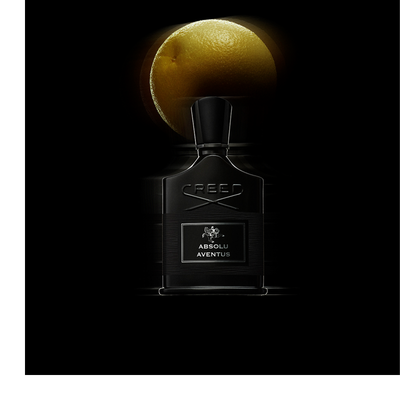 A dark bottle of Creed Absolu Aventus perfume with a rider on a horse logo, marked 75 ML 2.5FL.OZ., is tilted over two citrus fruits.