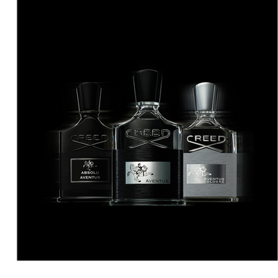 A dark bottle of Creed Absolu Aventus perfume with a rider on a horse logo, marked 75 ML 2.5FL.OZ., is tilted over two citrus fruits.