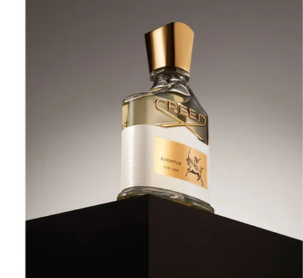 A Creed Aventus For Her perfume bottle with text AVENTUS FOR HER and a rider on a horse illustration on the label and CREED embossed on the bottle.