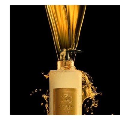 Golden liquid pours into a golden bottle, splashing and creating droplets against a black background, with a gold label featuring the text CREED 1760.