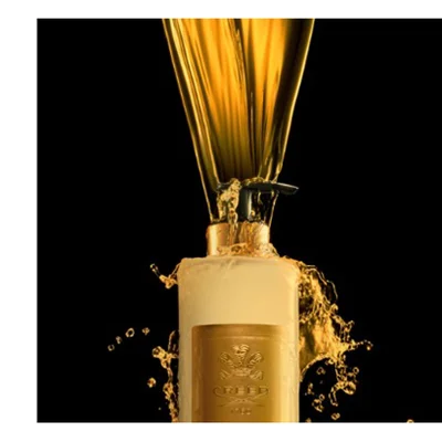 Golden liquid pours and splashes from a light-colored pump dispenser bottle featuring a gold label with an emblem and the text CREED 1760 against a black background