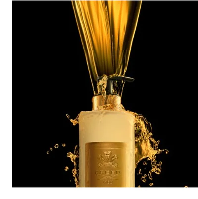 A dark brown perfume bottle with a gold cap and embossed gold text CREED and OUD ZARIAN is centered on a dark background between two dark, rough charred wood pieces.