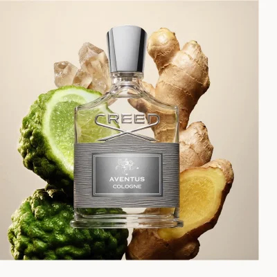 Creed Aventus Cologne bottle with ginger, citrus peel, woods, and green leaves displayed on a minimal white background.