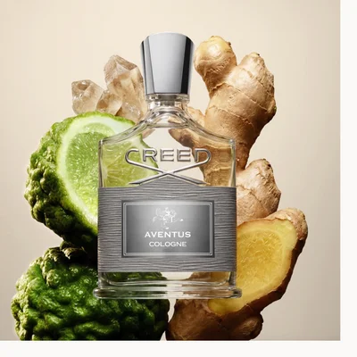 Creed Aventus Cologne bottle with ginger, citrus peel, woods, and green leaves on a minimal white background.