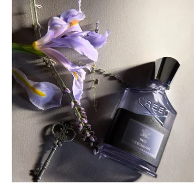 Perfume bottle labeled “Iris Debonair” beside purple flowers on a marble surface.